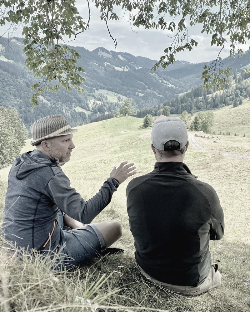 Tobias Frech und ein Kunde sitzen im Gespräch auf einer Wiese im Allgäu.